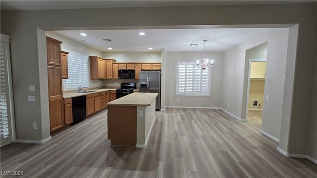 kitchen with light wood-type flooring, light countertops, black appliances, and an inviting chandelier