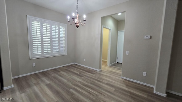 unfurnished dining area with baseboards, a notable chandelier, and wood finished floors