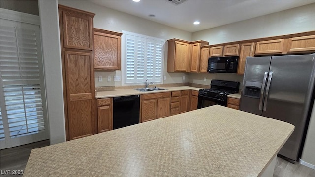 kitchen with wood finished floors, a sink, black appliances, light countertops, and recessed lighting