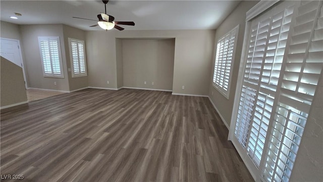 spare room featuring ceiling fan, baseboards, dark wood-type flooring, and a healthy amount of sunlight