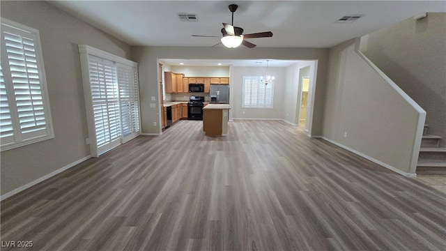 unfurnished living room with baseboards, visible vents, wood finished floors, and ceiling fan with notable chandelier