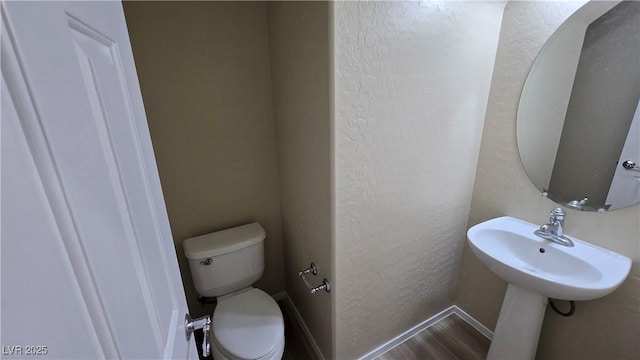 bathroom featuring a sink, toilet, a textured wall, and baseboards
