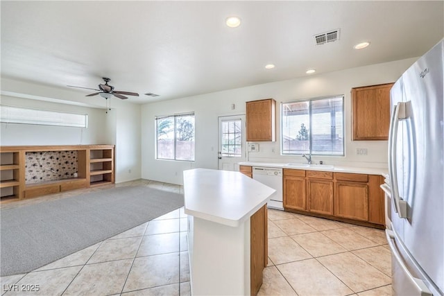 kitchen featuring a sink, freestanding refrigerator, brown cabinetry, light countertops, and white dishwasher