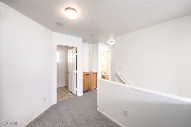 hallway featuring light carpet, baseboards, and an upstairs landing