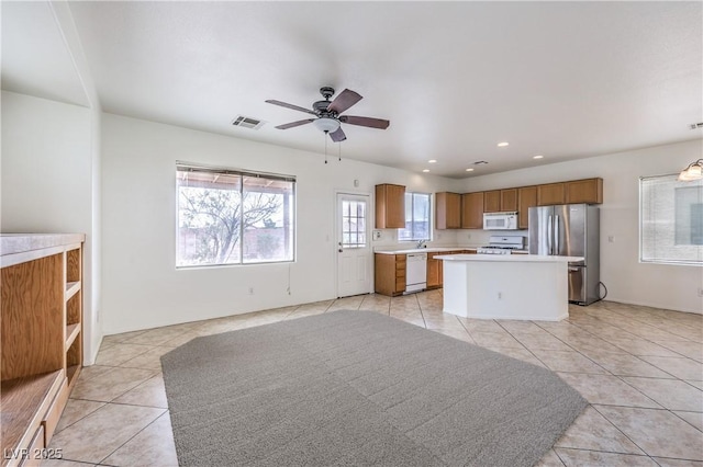 kitchen with light tile patterned floors, a center island, visible vents, white appliances, and light countertops