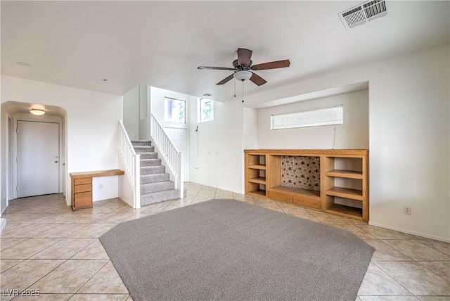 below grade area with light tile patterned floors, stairway, visible vents, and a ceiling fan