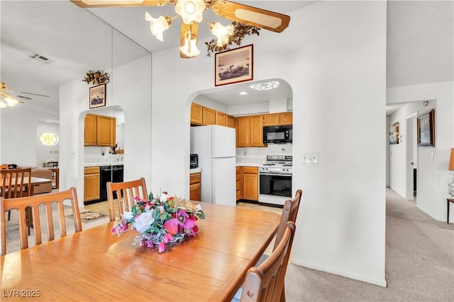 dining area with arched walkways, ceiling fan, light carpet, baseboards, and a chandelier