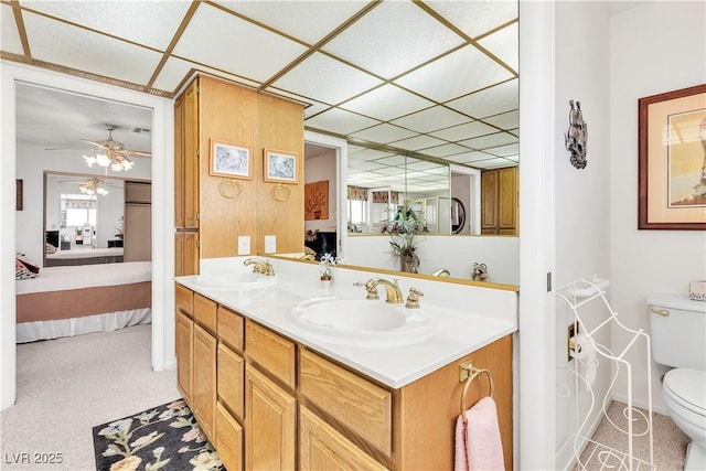 full bathroom with toilet, connected bathroom, a drop ceiling, double vanity, and a ceiling fan