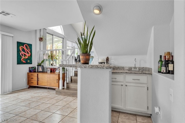 indoor wet bar with light tile patterned floors and vaulted ceiling
