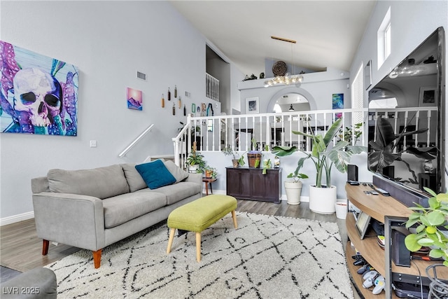 living area featuring wood finished floors, a chandelier, baseboards, high vaulted ceiling, and stairway
