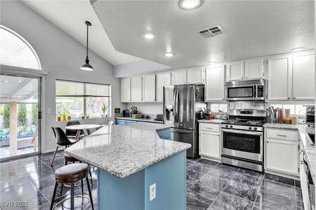 kitchen featuring appliances with stainless steel finishes, a textured ceiling, a kitchen island, vaulted ceiling, and light stone countertops