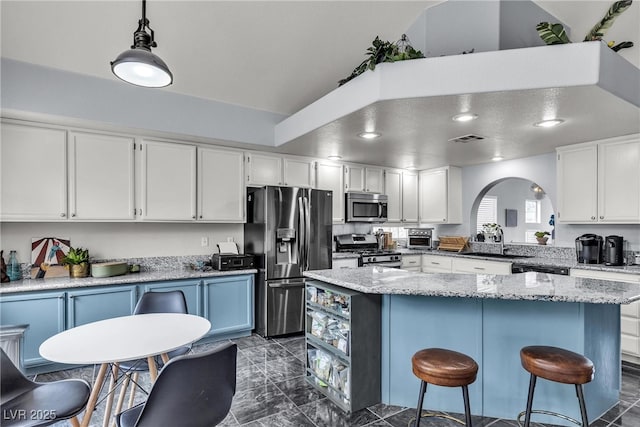 kitchen with appliances with stainless steel finishes, a sink, arched walkways, a kitchen island, and white cabinets