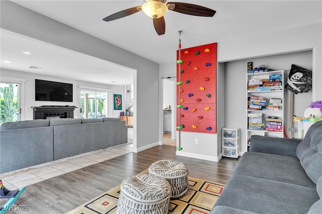 living area with ceiling fan, healthy amount of natural light, wood finished floors, a brick fireplace, and recessed lighting