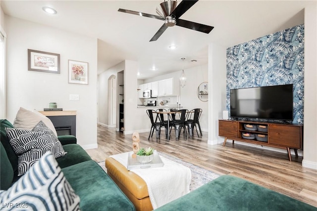 living room featuring ceiling fan, light wood finished floors, baseboards, recessed lighting, and arched walkways