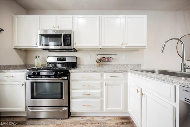 kitchen with appliances with stainless steel finishes, a sink, white cabinets, light wood-type flooring, and light countertops