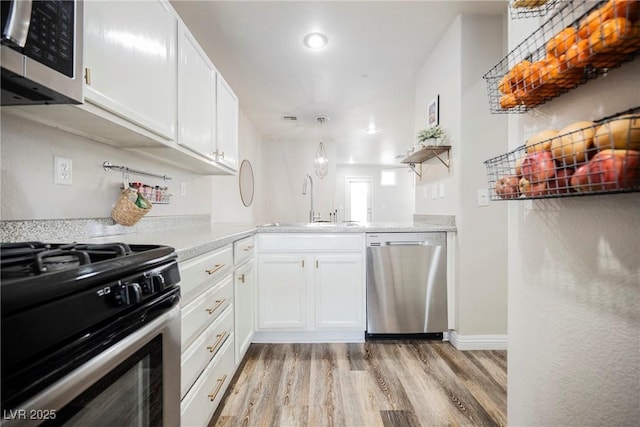kitchen featuring stainless steel appliances, a sink, light wood-style flooring, and white cabinetry