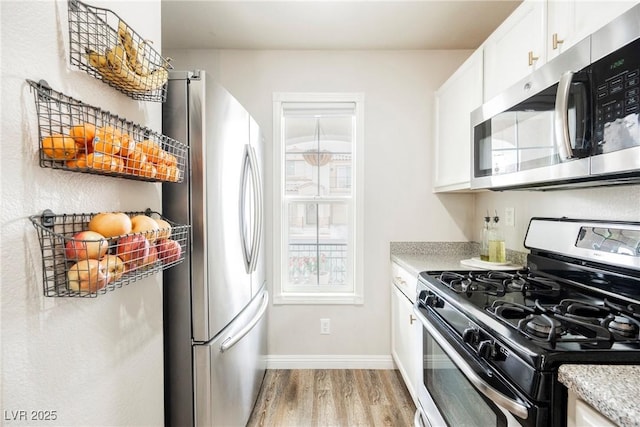 kitchen with stainless steel appliances, light wood-style flooring, baseboards, and white cabinets