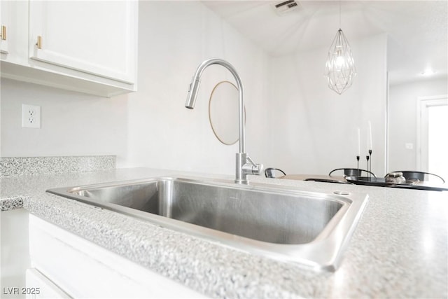 kitchen view of a sink, white cabinetry, light countertops, and hanging light fixtures