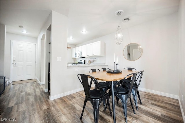dining space featuring wood finished floors, baseboards, and arched walkways