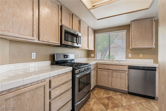 4517 Rodman Dr, Las Vegas, NV 89130 - kitchen with appliances with stainless steel finishes, light brown cabinetry, light tile patterned floors, a sink, and tile countertops