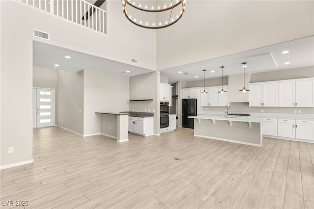 unfurnished living room with baseboards, a sink, a towering ceiling, light wood-style floors, and a chandelier