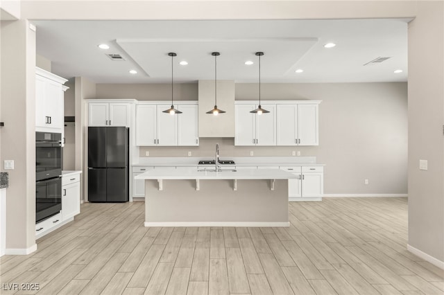 kitchen featuring black appliances, baseboards, light countertops, a kitchen bar, and light wood-type flooring