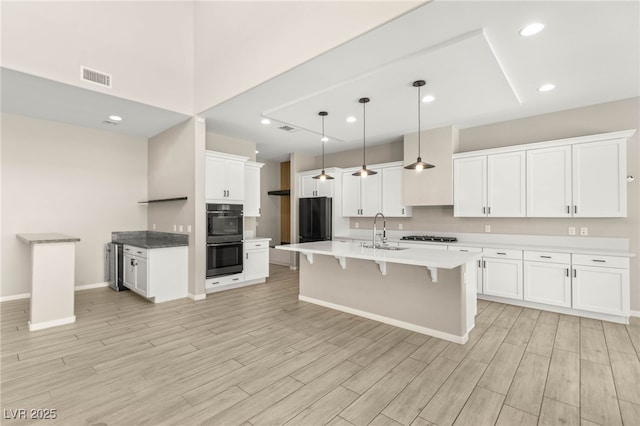 kitchen with black appliances, a sink, a kitchen breakfast bar, light wood-style flooring, and white cabinets