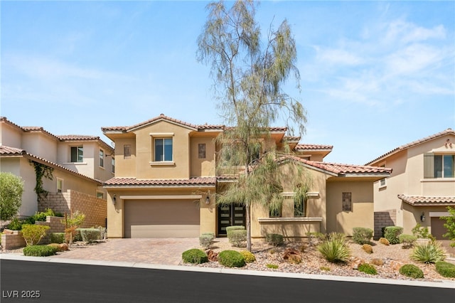 mediterranean / spanish home with stucco siding, decorative driveway, a tile roof, and a garage