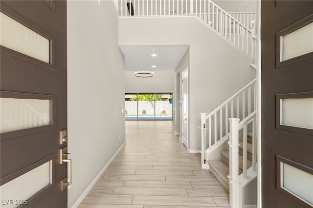 entrance foyer featuring stairway, baseboards, light wood-style floors, a high ceiling, and a chandelier