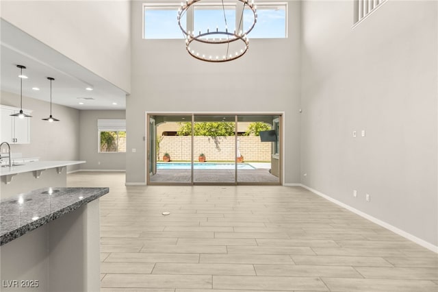 unfurnished living room with a high ceiling, a chandelier, baseboards, light wood-style flooring, and a sink