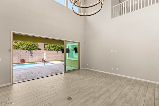 empty room featuring a towering ceiling, a chandelier, wood finished floors, and baseboards