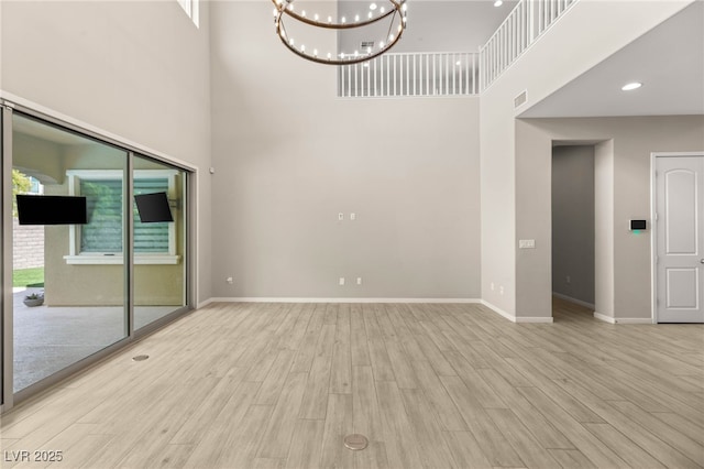 unfurnished living room with a towering ceiling, a chandelier, wood finished floors, baseboards, and recessed lighting