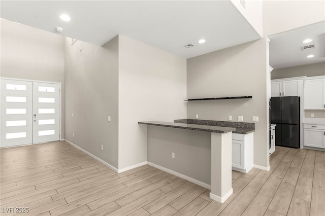 kitchen with freestanding refrigerator, white cabinets, light wood-style flooring, dark stone countertops, and recessed lighting