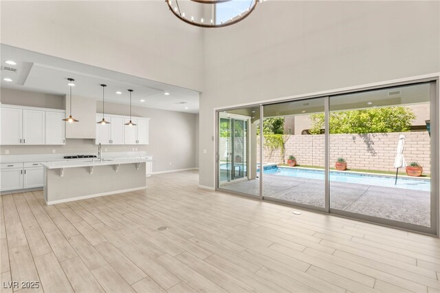 unfurnished living room featuring light wood-style flooring, baseboards, a sink, a towering ceiling, and recessed lighting