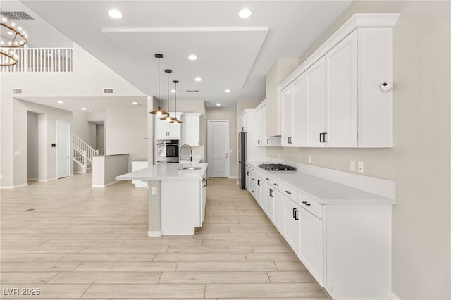 kitchen with appliances with stainless steel finishes, light wood finished floors, light countertops, white cabinets, and a kitchen island with sink