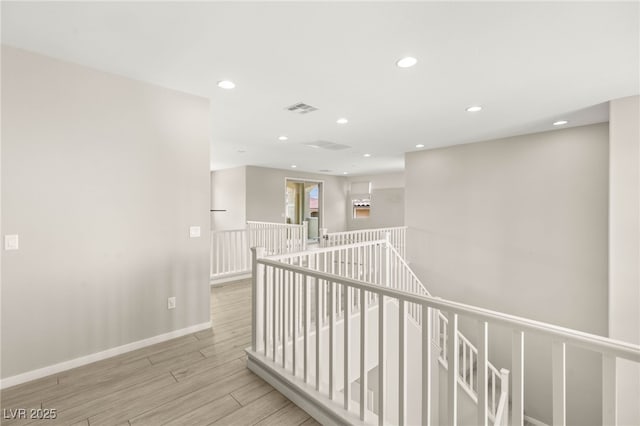 corridor with an upstairs landing, wood finished floors, recessed lighting, and baseboards