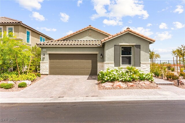 mediterranean / spanish home with stone siding, an attached garage, stucco siding, decorative driveway, and fence