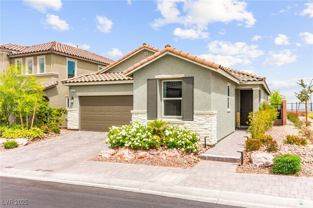 mediterranean / spanish-style home with a garage, stone siding, stucco siding, and driveway