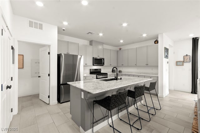 kitchen with appliances with stainless steel finishes, a sink, gray cabinetry, a breakfast bar area, and a center island with sink