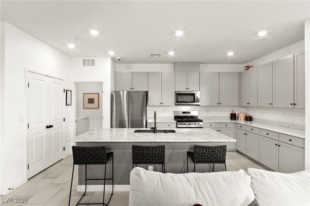 kitchen with stainless steel appliances, a sink, gray cabinets, a kitchen breakfast bar, and recessed lighting