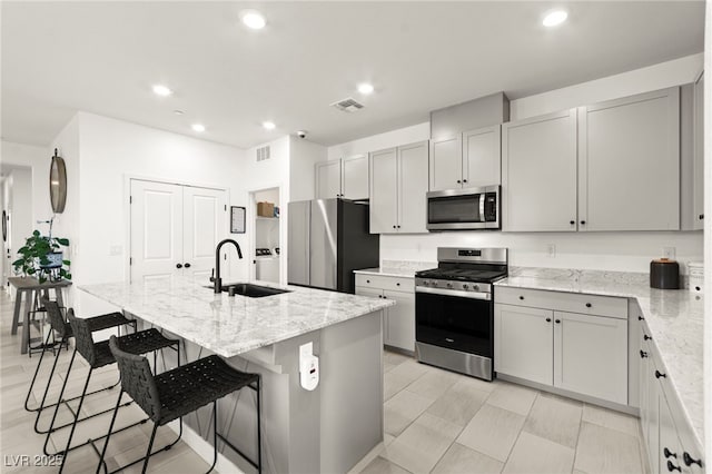 kitchen featuring appliances with stainless steel finishes, a sink, light stone counters, a kitchen bar, and recessed lighting