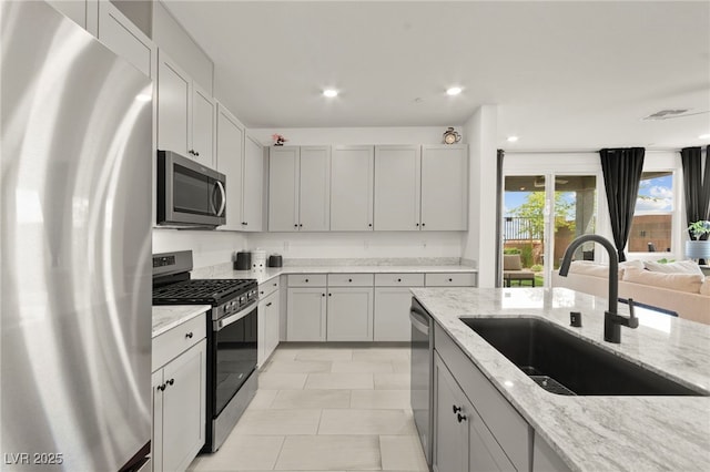 kitchen with stainless steel appliances, a sink, light stone counters, open floor plan, and recessed lighting