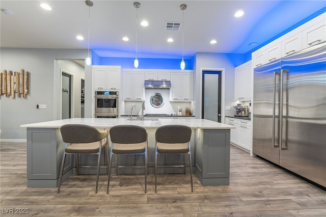 5865 Alice Landing Ct, Las Vegas, NV 89149 - kitchen featuring appliances with stainless steel finishes, under cabinet range hood, white cabinets, a spacious island, and wood finished floors
