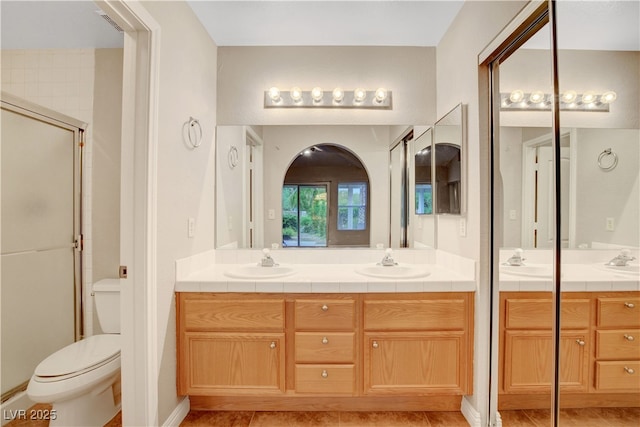 full bath with double vanity, toilet, and a shower with shower door