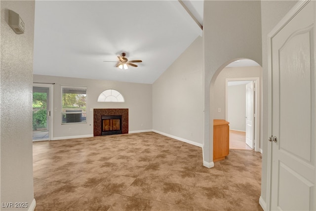 unfurnished living room with a ceiling fan, arched walkways, vaulted ceiling, a fireplace, and baseboards