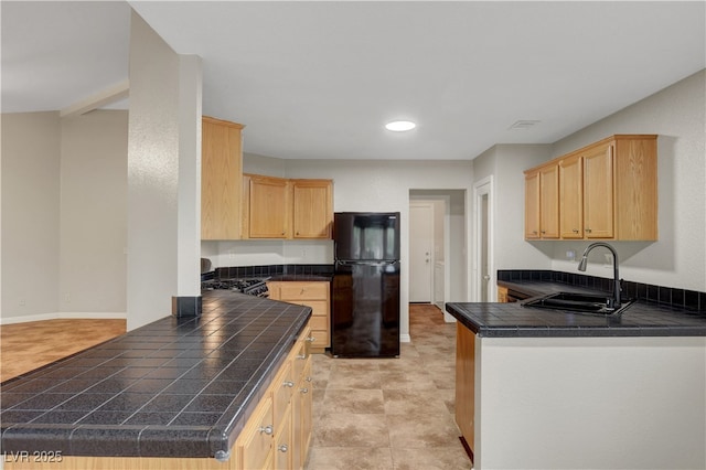 kitchen with freestanding refrigerator, a sink, light brown cabinetry, a peninsula, and gas range oven