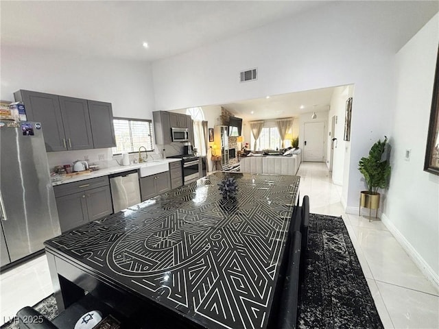 kitchen with stainless steel appliances, high vaulted ceiling, light countertops, gray cabinets, and a sink