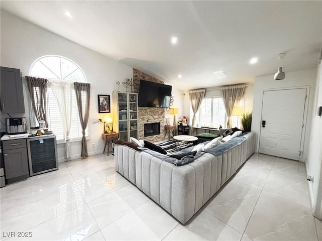 living area with beverage cooler, a stone fireplace, vaulted ceiling, light marble finish floors, and recessed lighting