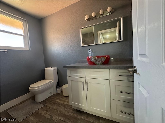 bathroom with toilet, vanity, wood finished floors, a textured ceiling, and baseboards