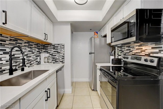 kitchen featuring stainless steel appliances, a sink, white cabinetry, light tile patterned flooring, and a raised ceiling
